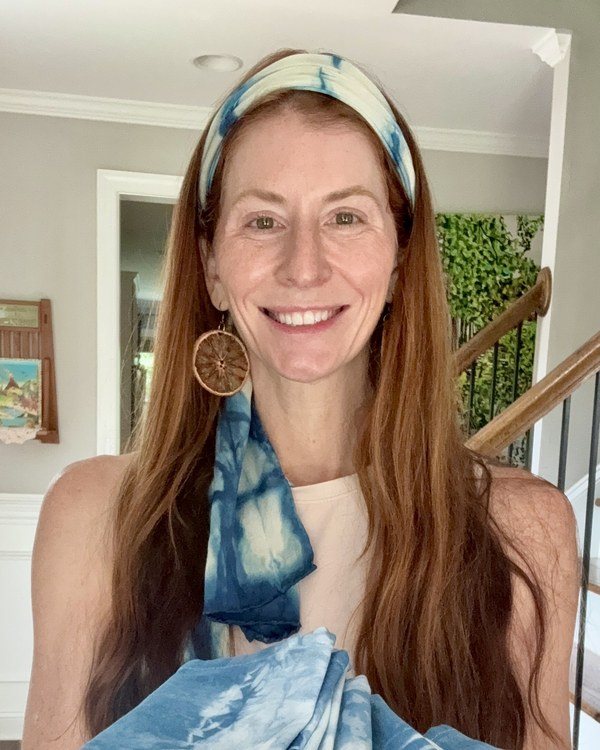 Kristi Thompson wearing an indigo headband and scarf and holding her finished shibori napkins