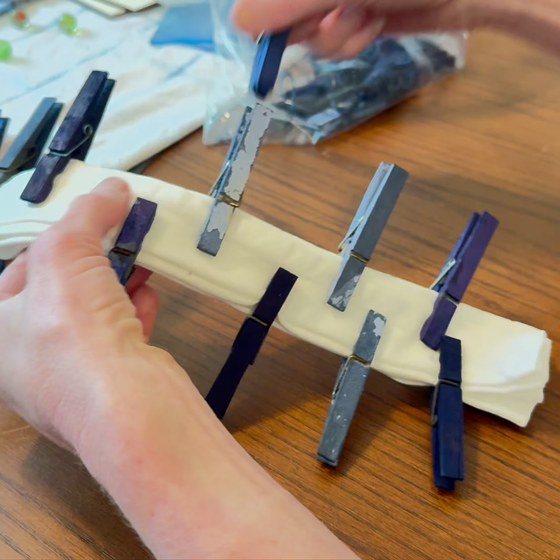 Kristi's hands holding an accordion-folded white napkin clamped with clothespins